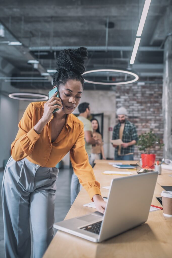 Focused girl talking on smartphone near laptop